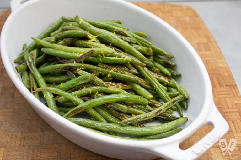 Serving dish with roasted green beans and lemon zest.