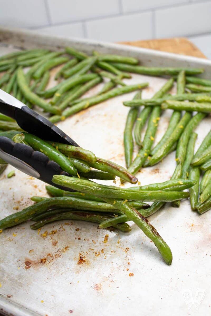 Grabbing roasted green beans from a sheet pan with tongs.
