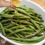 Squeezing a lemon wedge over a platter of roasted green beans.