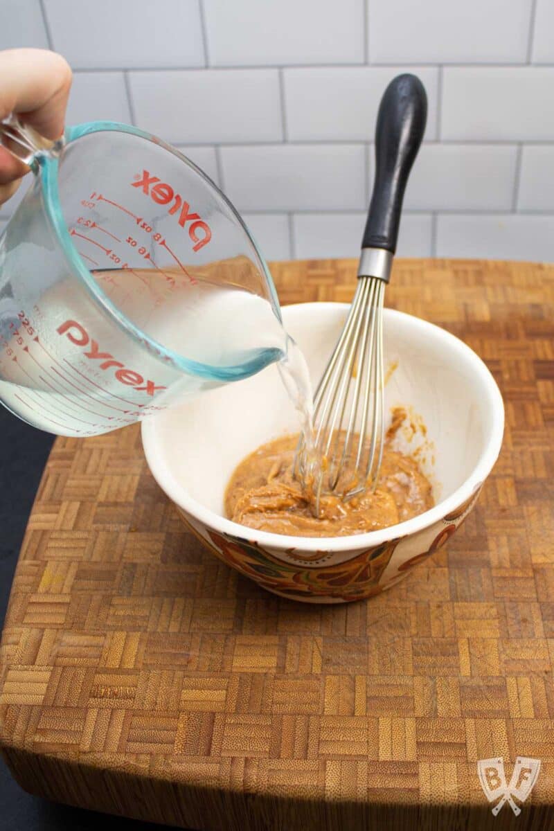 Pouring reserved pasta water into a bowl of peanut butter.