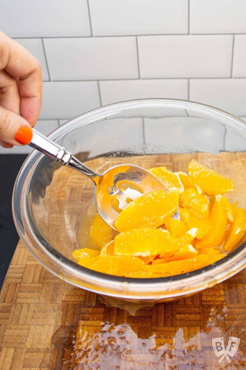 Stirring orange segments in a bowl of spiced honey.