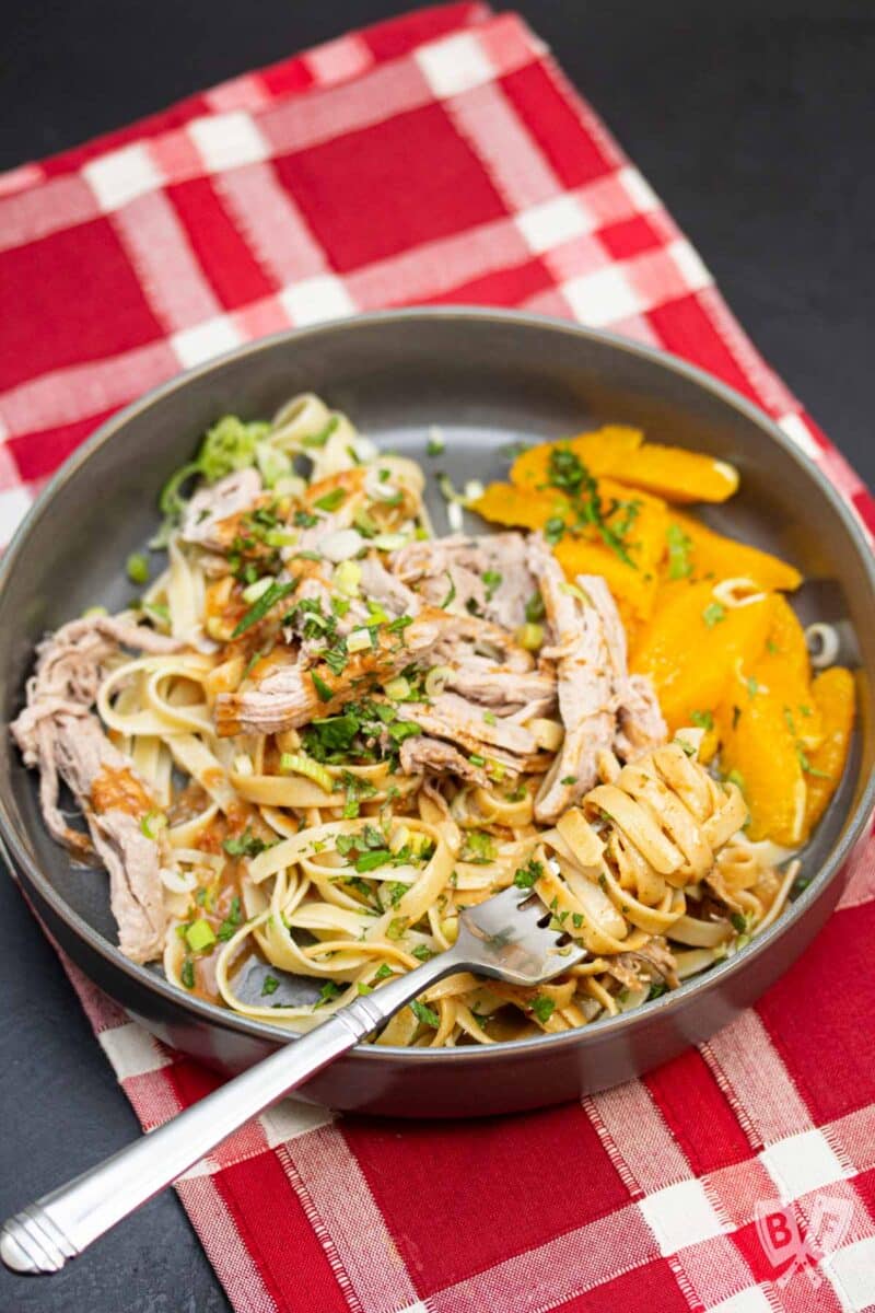 Fork twirling peanut noodles served with pork tenderloin and oranges.