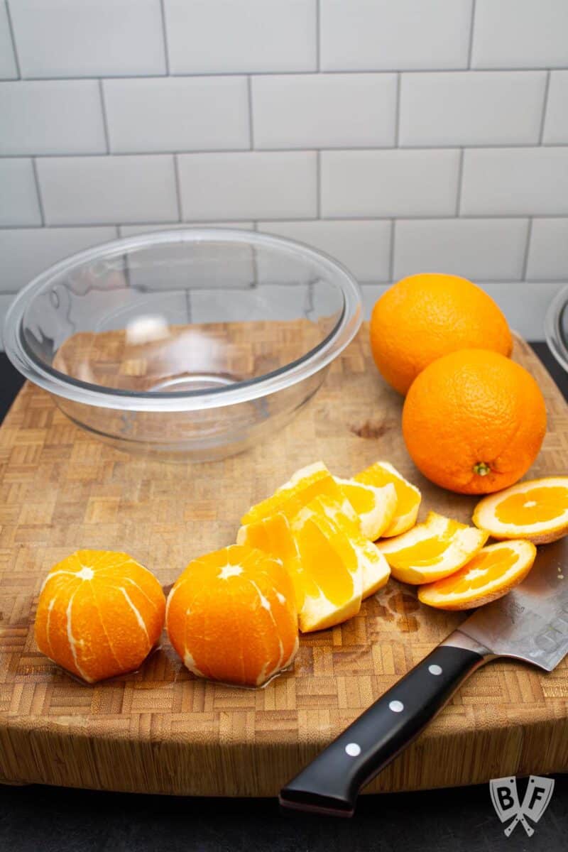 Oranges on a cutting board with a knife and a bowl.