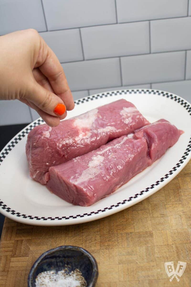 Sprinkling salt onto 2 pieces of pork tenderloin.