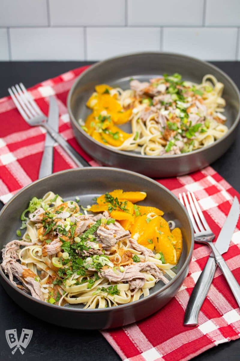 2 bowls of pork and peanut noodles with oranges.