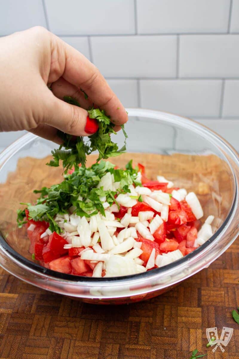 Adding cilantro to a bowl of pico de gallo ingredients.