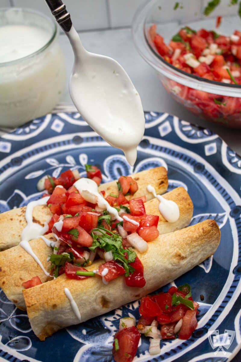 Spooning lime crema over baked taquitos.