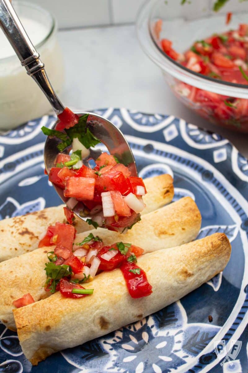 Spooning pico de gallo over baked taquitos.