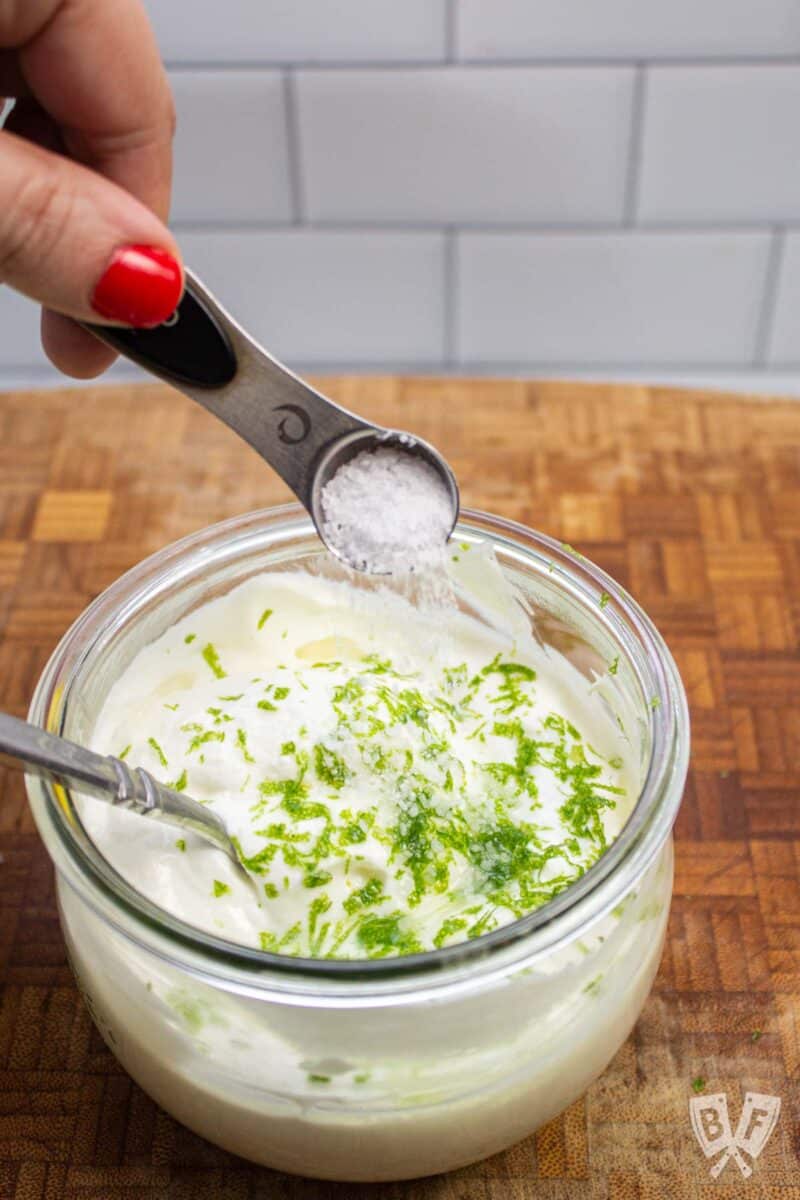 Adding salt to a bowl of Greek yogurt and lime zest.