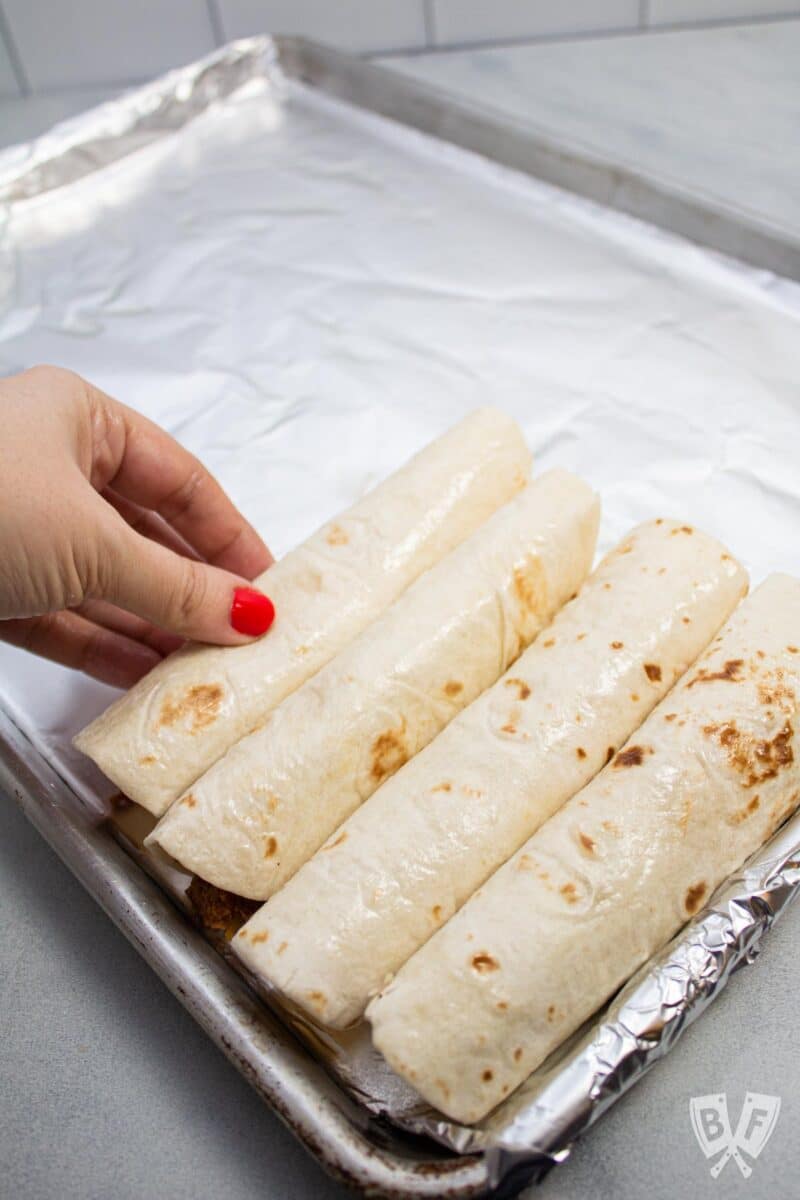 Adding rolled taquitos to a foil-lined baking sheet.