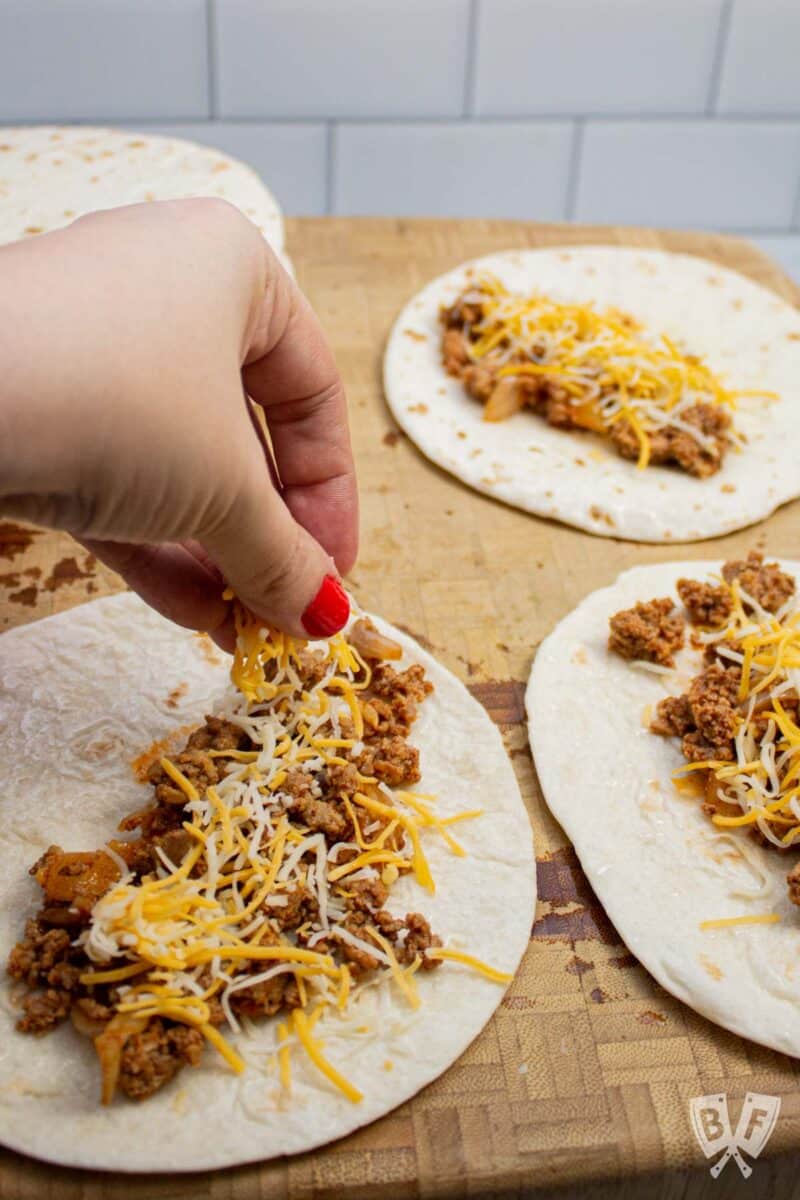 Sprinkling cheese onto tortillas topped with taquito filling.