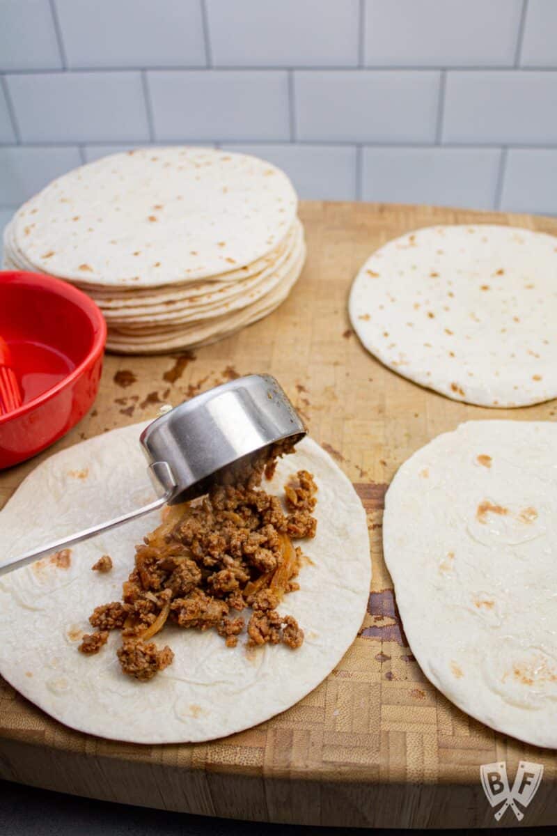 Spreading taquito mixture onto a tortilla.