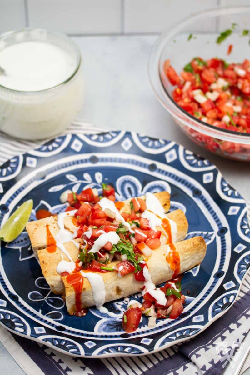 Plate of baked taquitos with pico de gallo and lime crema.