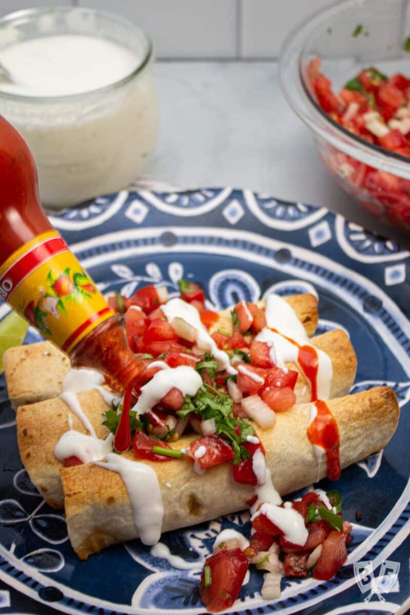 Pouring hot sauce over baked taquitos.