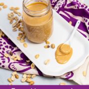 Platter with a jar of homemade peanut butter with peanuts scattered around and a spoon resting in a pile of peanut butter. Text reads "Easy Homemade Peanut Butter bigflavorstinykitchen.com".