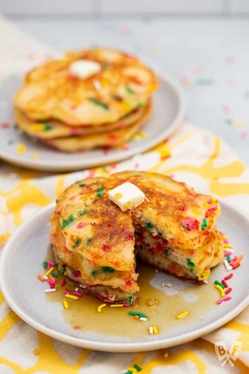 Stack of funfetti pancakes on a plate with a slice taken out of them.