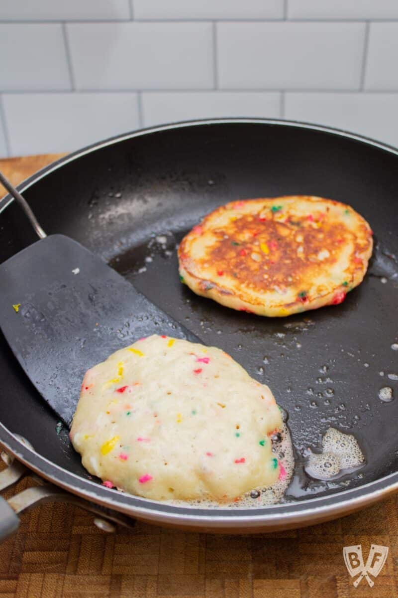 Flipping funfetti pancakes in a skillet.