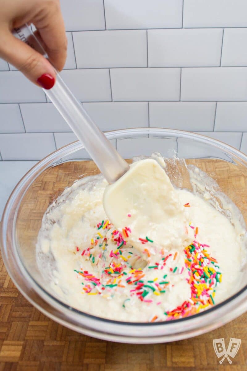 Stirring rainbow sprinkles into a bowl of pancake batter.