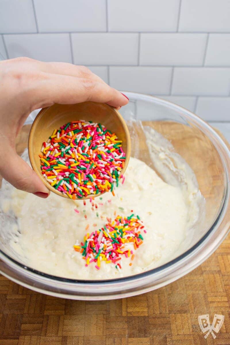 Adding rainbow sprinkles to a bowl of pancake batter.