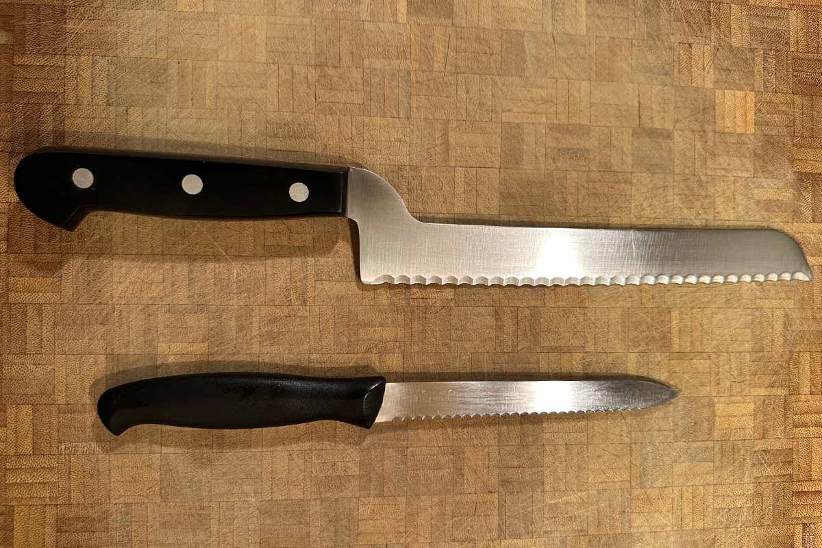 Two serrated knives on a cutting board.