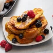 Plates of challah french toast with powdered sugar, fresh berries, and maple syrup.