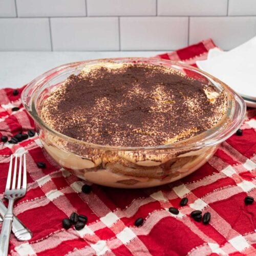 Homemade tiramisu in a serving dish with plates and forks for serving.