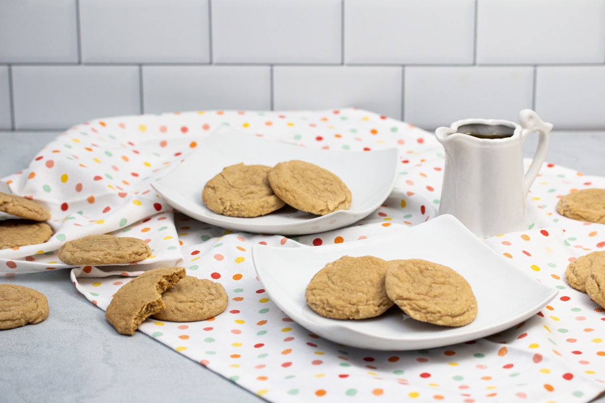 Maple cookies on plates with a pitcher of maple syrup alongside.