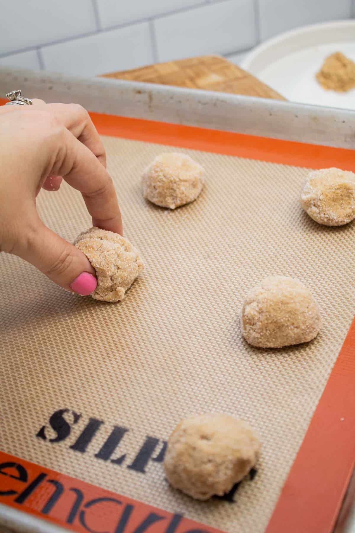 Placing maple cookie dough balls onto a lined baking sheet.
