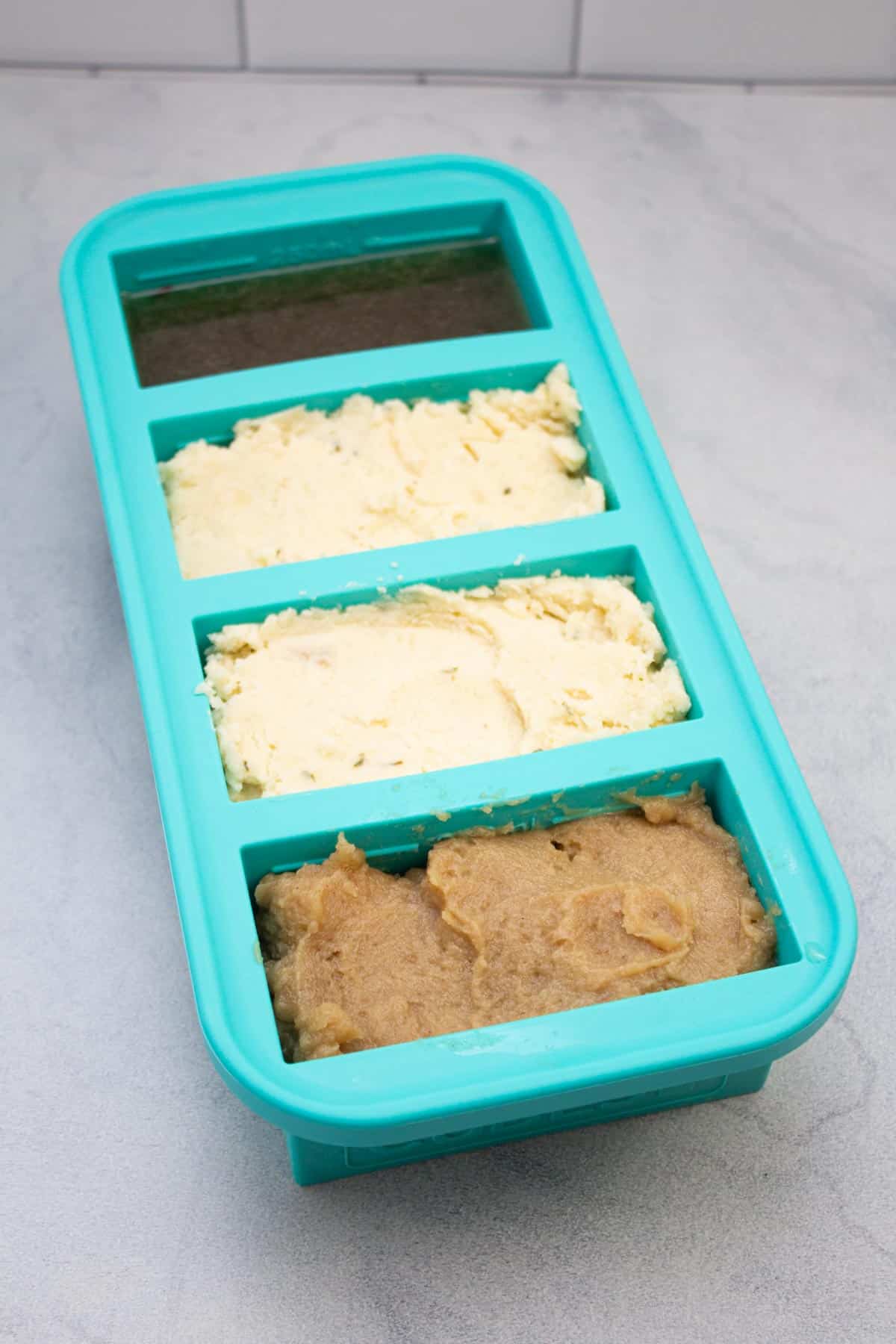Portioned silicone freezer tray filled with various food.