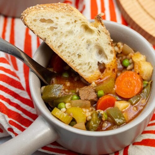 Two bowls of old fashioned beef stew with sliced bread served alongside.