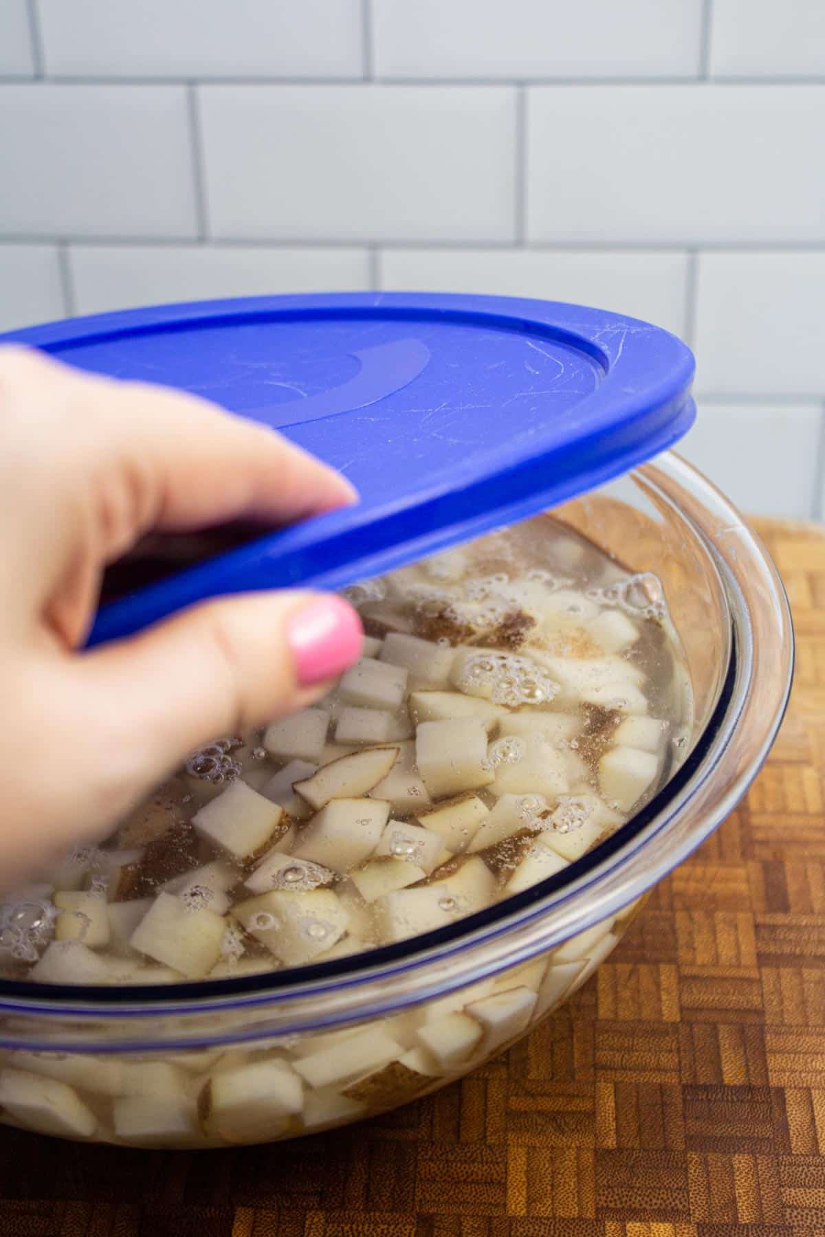 Putting a lid on a bowl of diced potatoes in water.