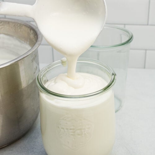 Ladling homemade yogurt into a glass jar for storage.
