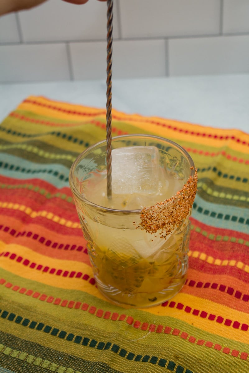 Stirring a passionfruit margarita in a Tajin-rimmed cocktail glass.