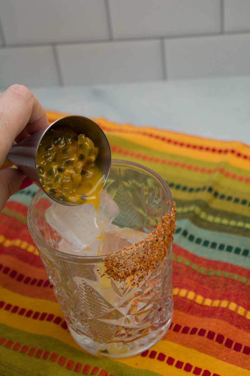Pouring fresh passionfruit pulp into a cocktail glass.