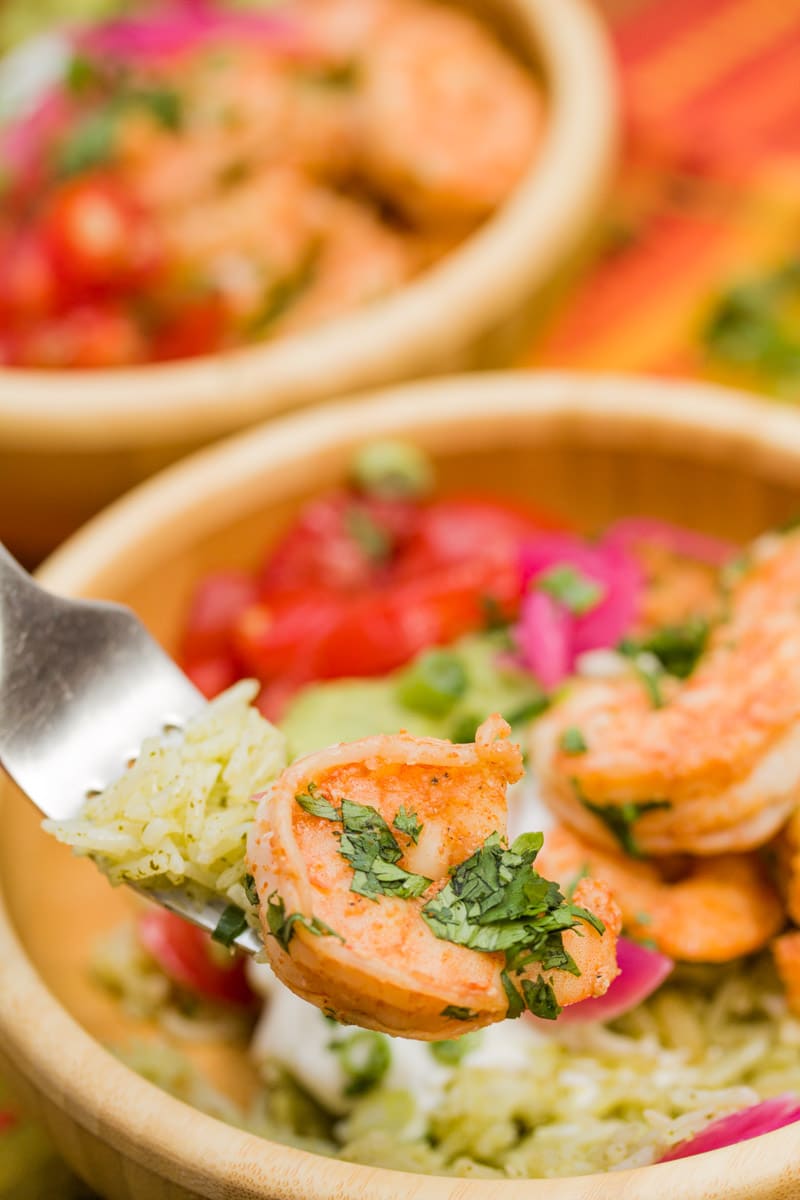 Bowl of sautéed shrimp with pickled onions, cilantro rice, guacamole, tomatoes, and sour cream.