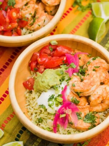 Bowl of sautéed shrimp with pickled onions, cilantro rice, guacamole, tomatoes, and sour cream.