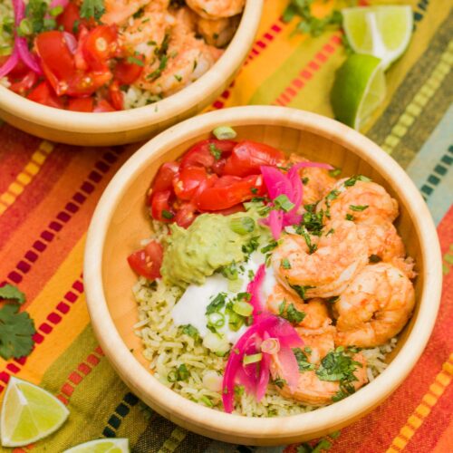 Bowl of sautéed shrimp with pickled onions, cilantro rice, guacamole, tomatoes, and sour cream.
