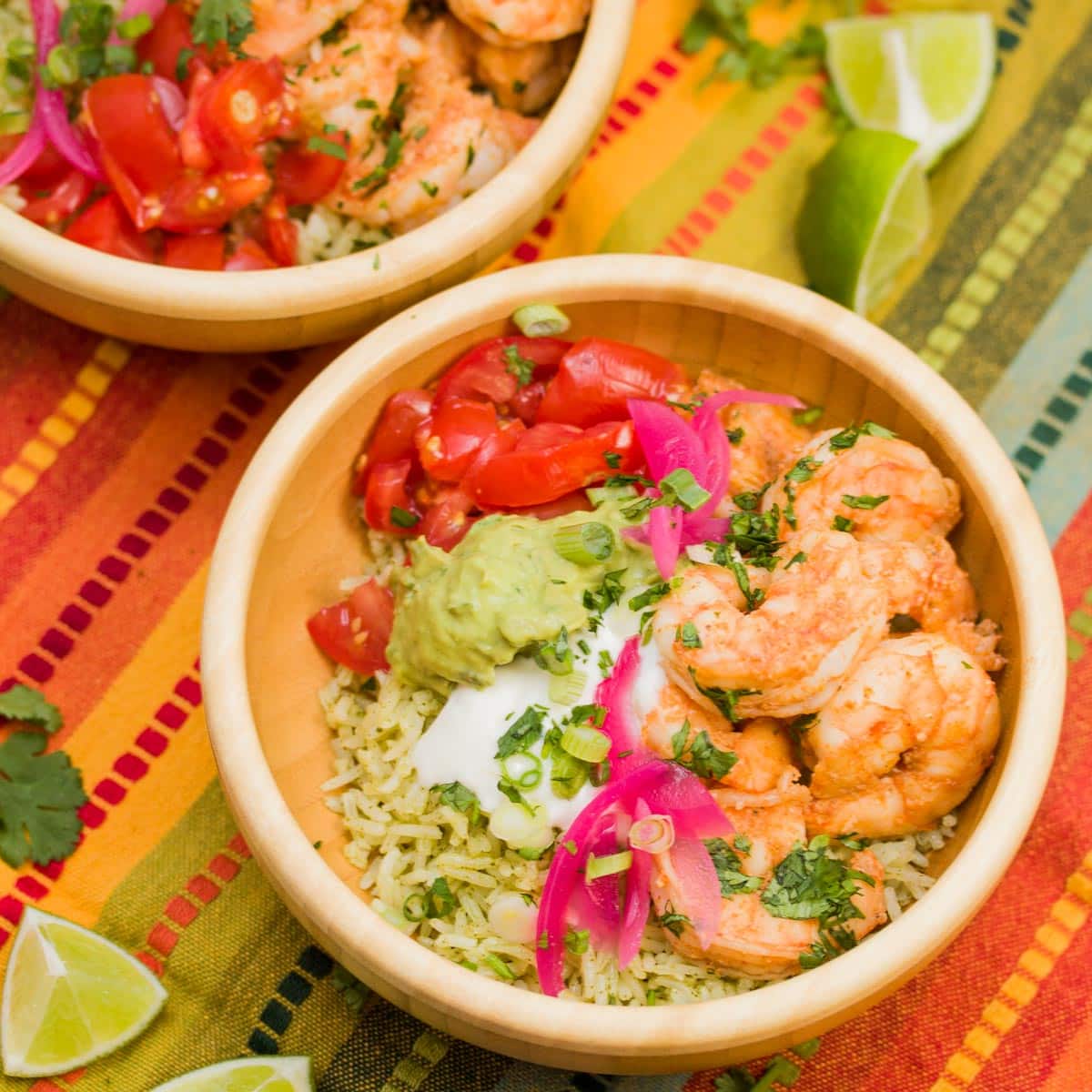 Bowl of sautéed shrimp with pickled onions, cilantro rice, guacamole, tomatoes, and sour cream.