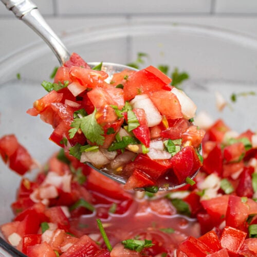 Spoon scooping up pico de gallo from a bowl.