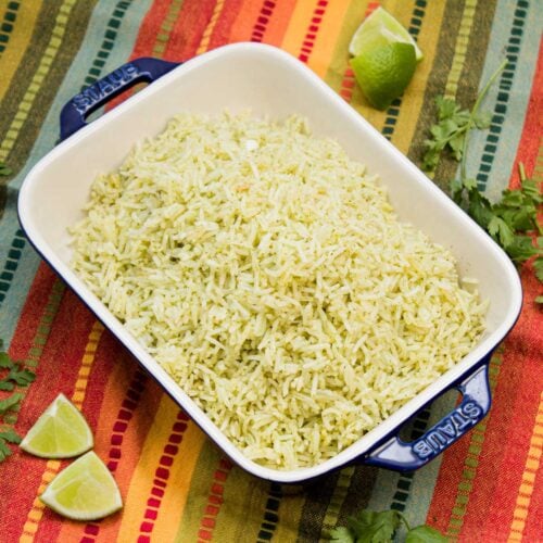 Serving dish of cilantro lime rice with lime wedges and cilantro sprigs alongside.