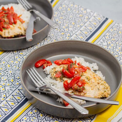 Two shallow bowls with rice and chicken paillards topped with tomato-dill relish.