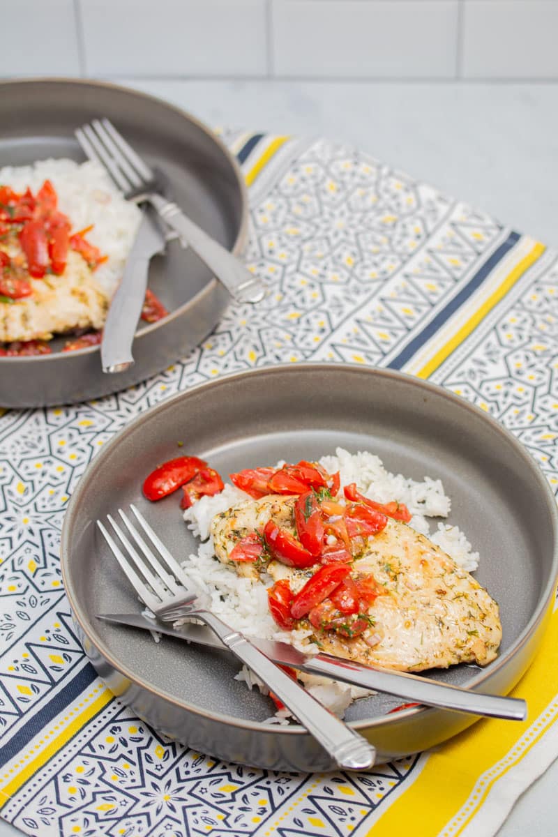 Two shallow bowls with rice and chicken paillards topped with tomato-dill relish.