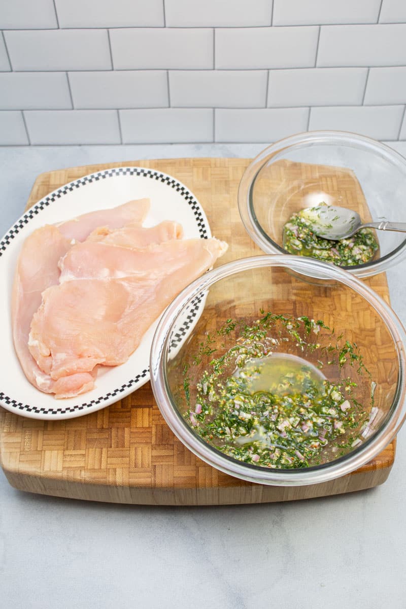 A plate of thin chicken breasts with 2 bowls of mustard dill vinaigrette.