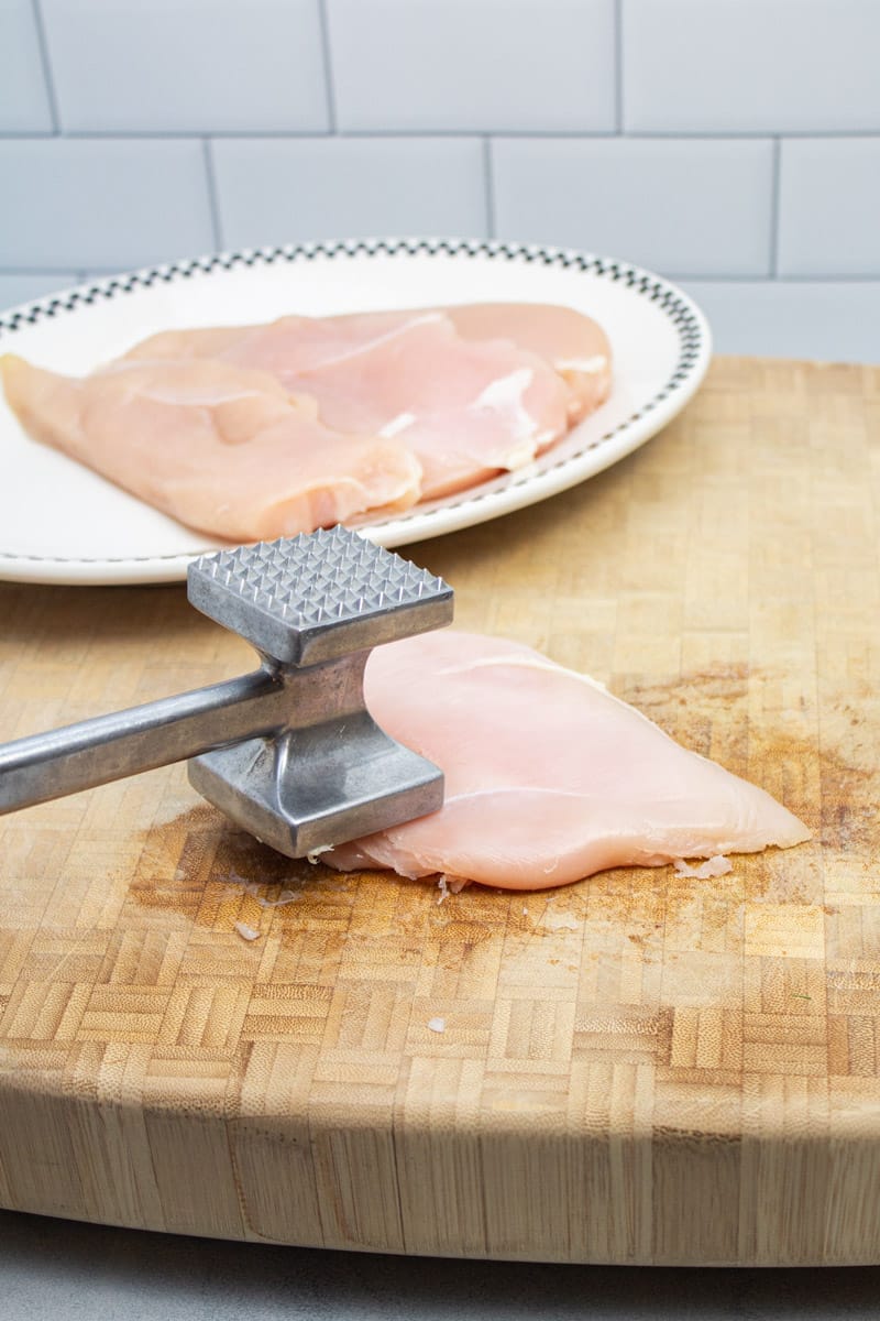 Pounding chicken breasts with a meat mallet.