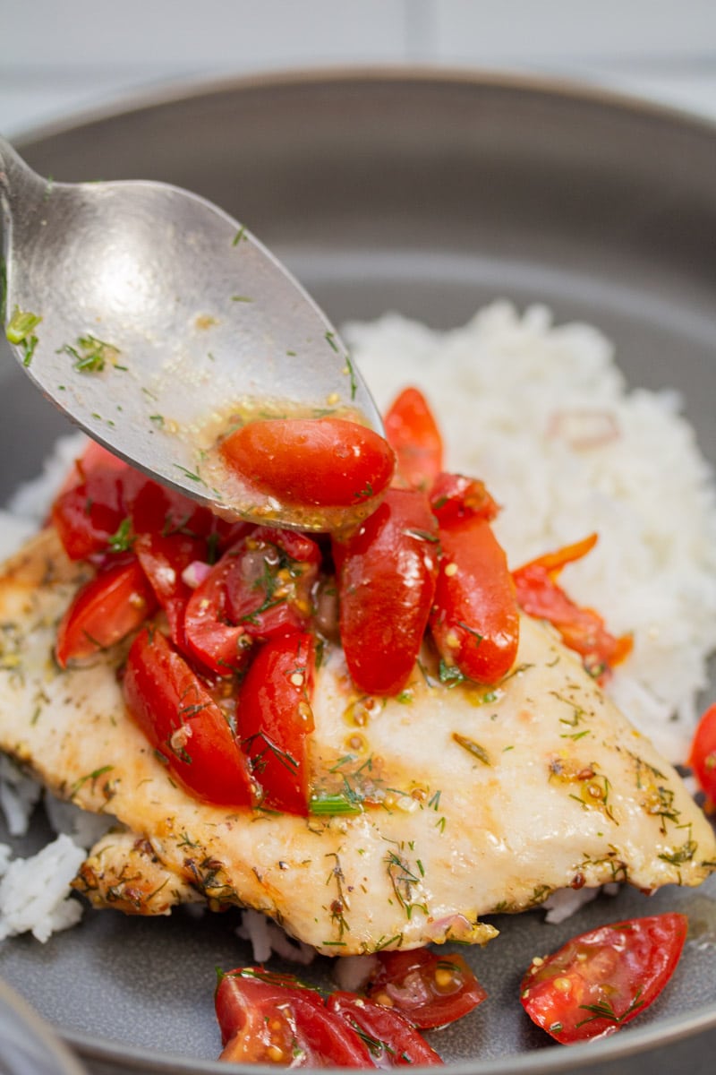 Spooning tomato dill relish over a cooked chicken cutlet and rice.