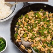 Cast iron skillet of chicken and bell pepper stir-fry with rice and green onions alongside.