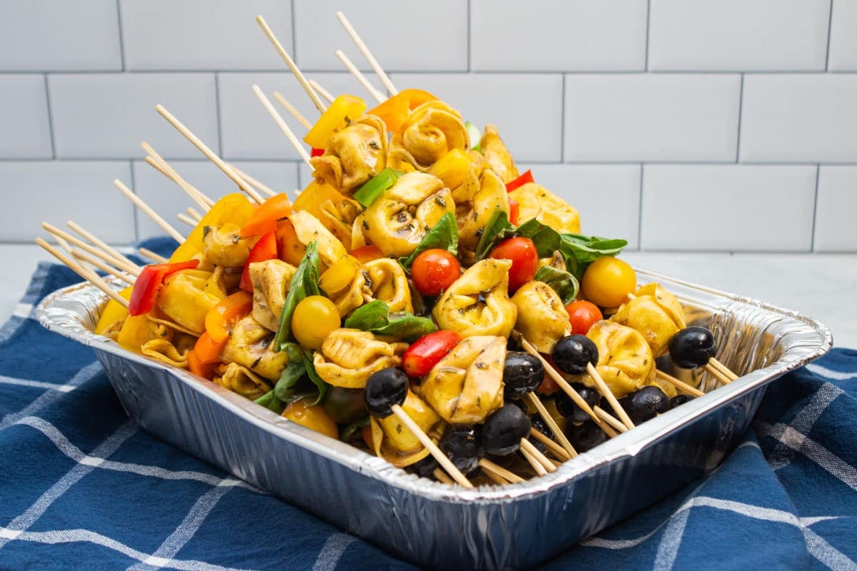 A tray of pasta salad skewers with tortellini, bell peppers, tomatoes, basil, and black olives.