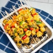 A tray of pasta salad skewers with tortellini, bell peppers, tomatoes, basil, and black olives.