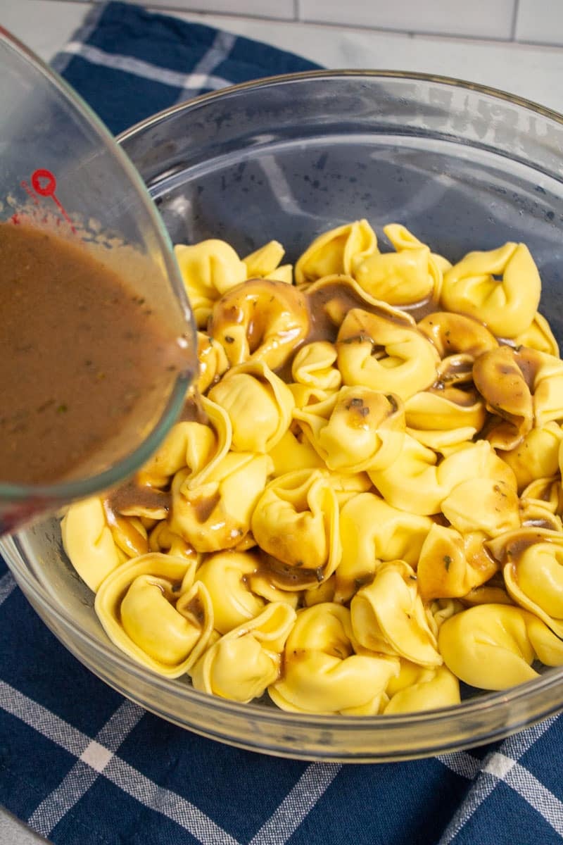 Pouring balsamic vinaigrette into a bowl of cooked tortelloni.