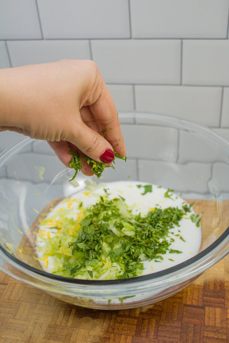 Adding chopped green onions to a bowl of yogurt and cucumber.